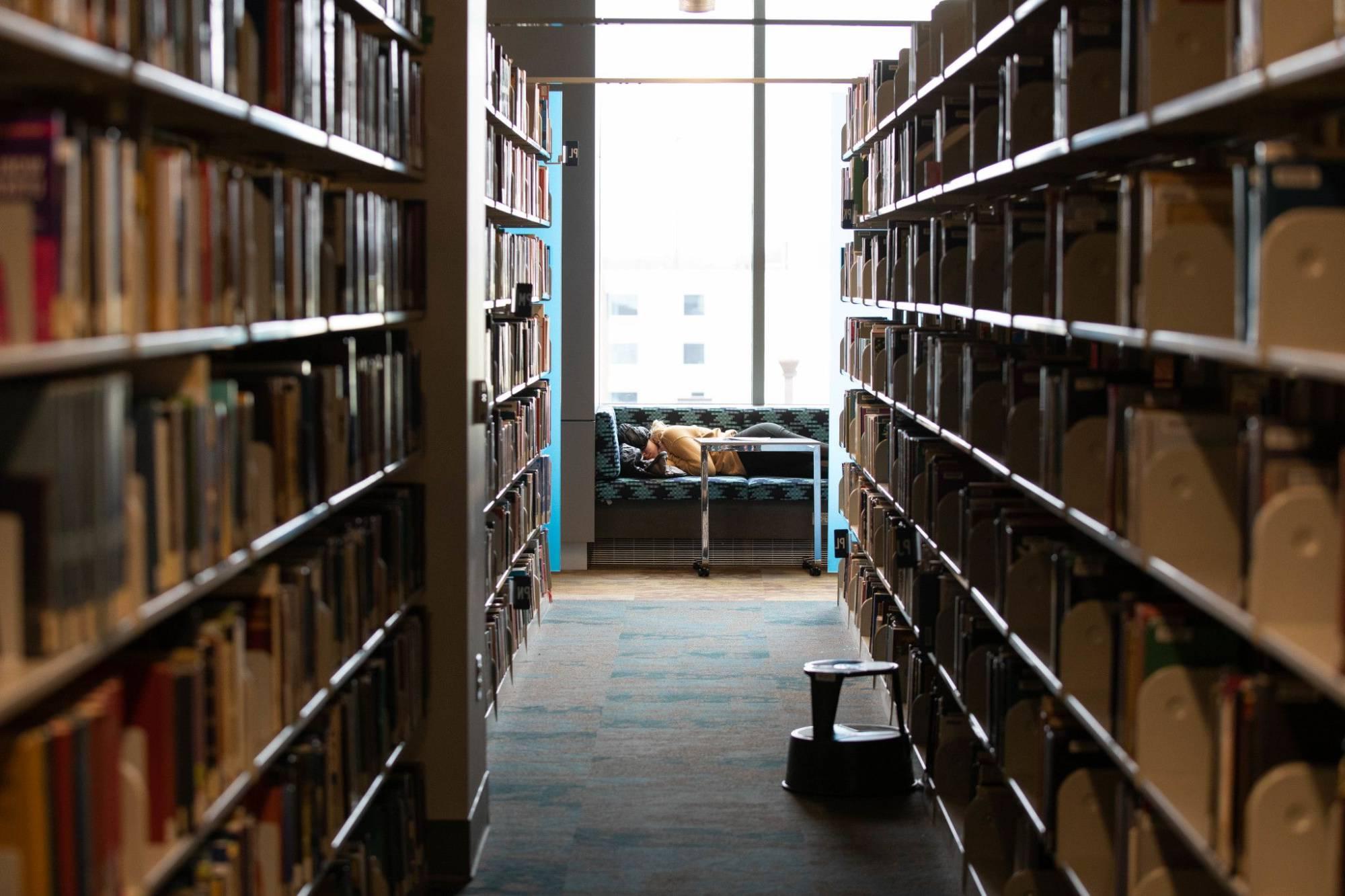 Person sleeping on library sofa at the end of hallway of bookshelves